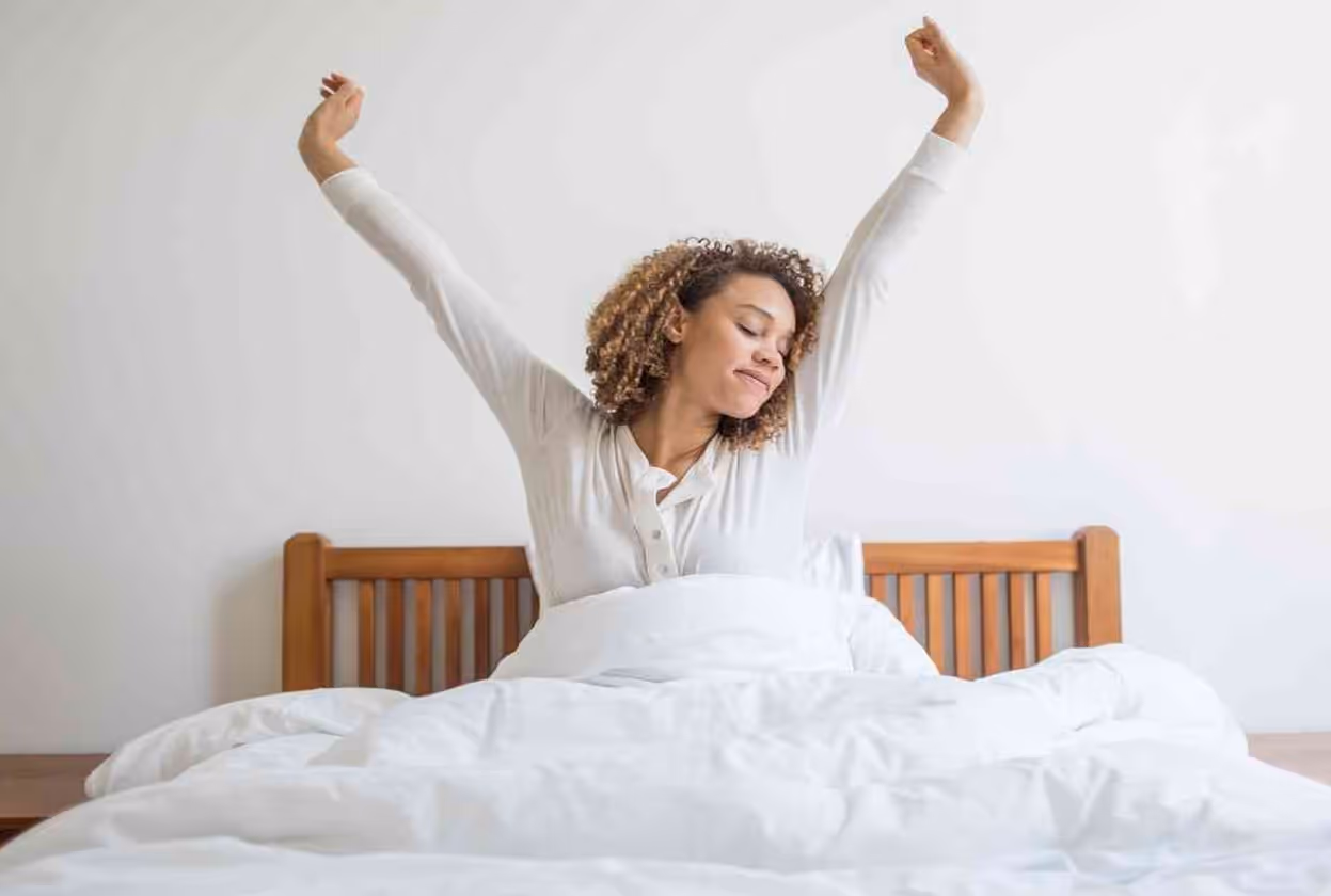 Woman with curly hair in bed stretching her arms