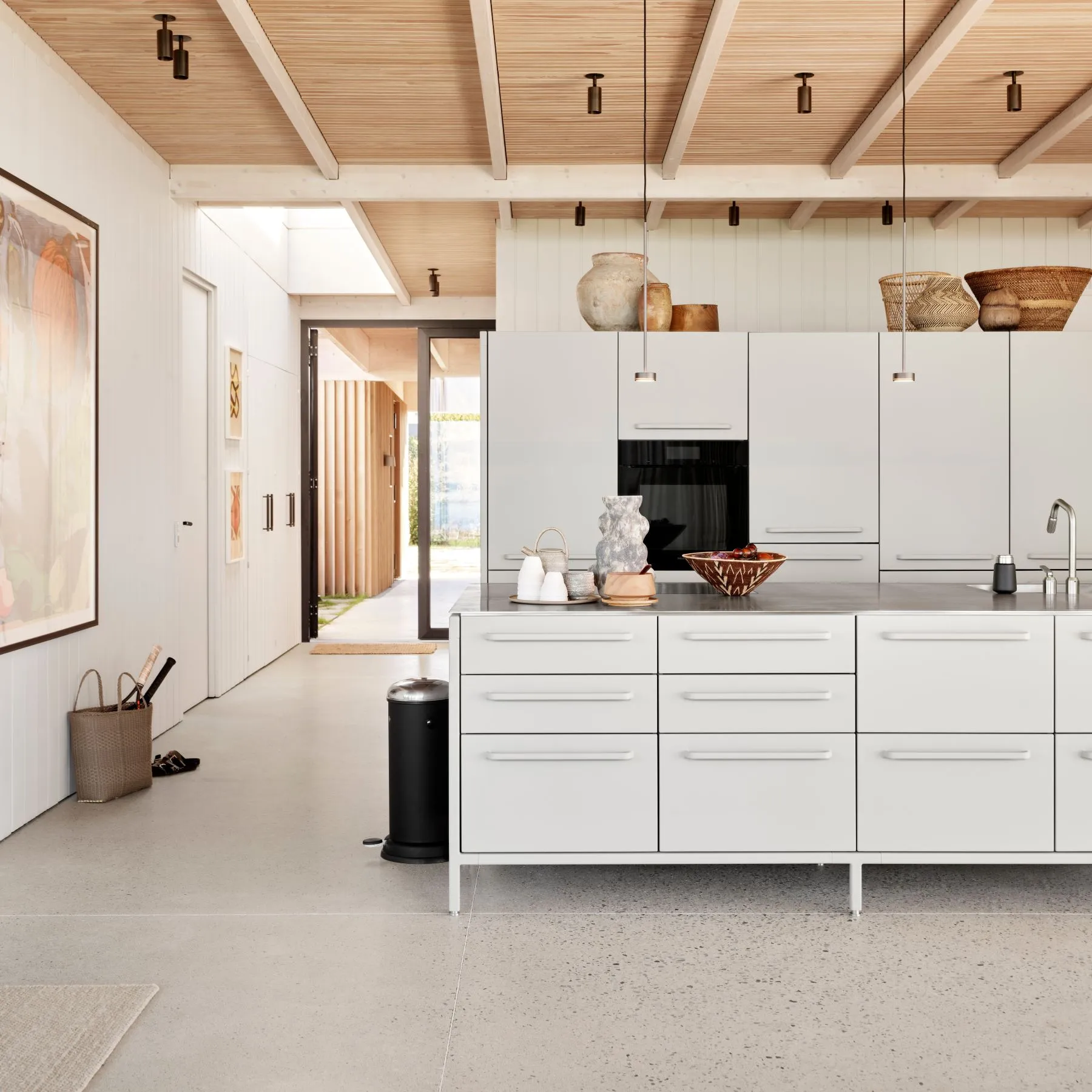 Modern kitchen with white cabinets, island with decorative vases, hanging lights, and wooden ceiling beams.