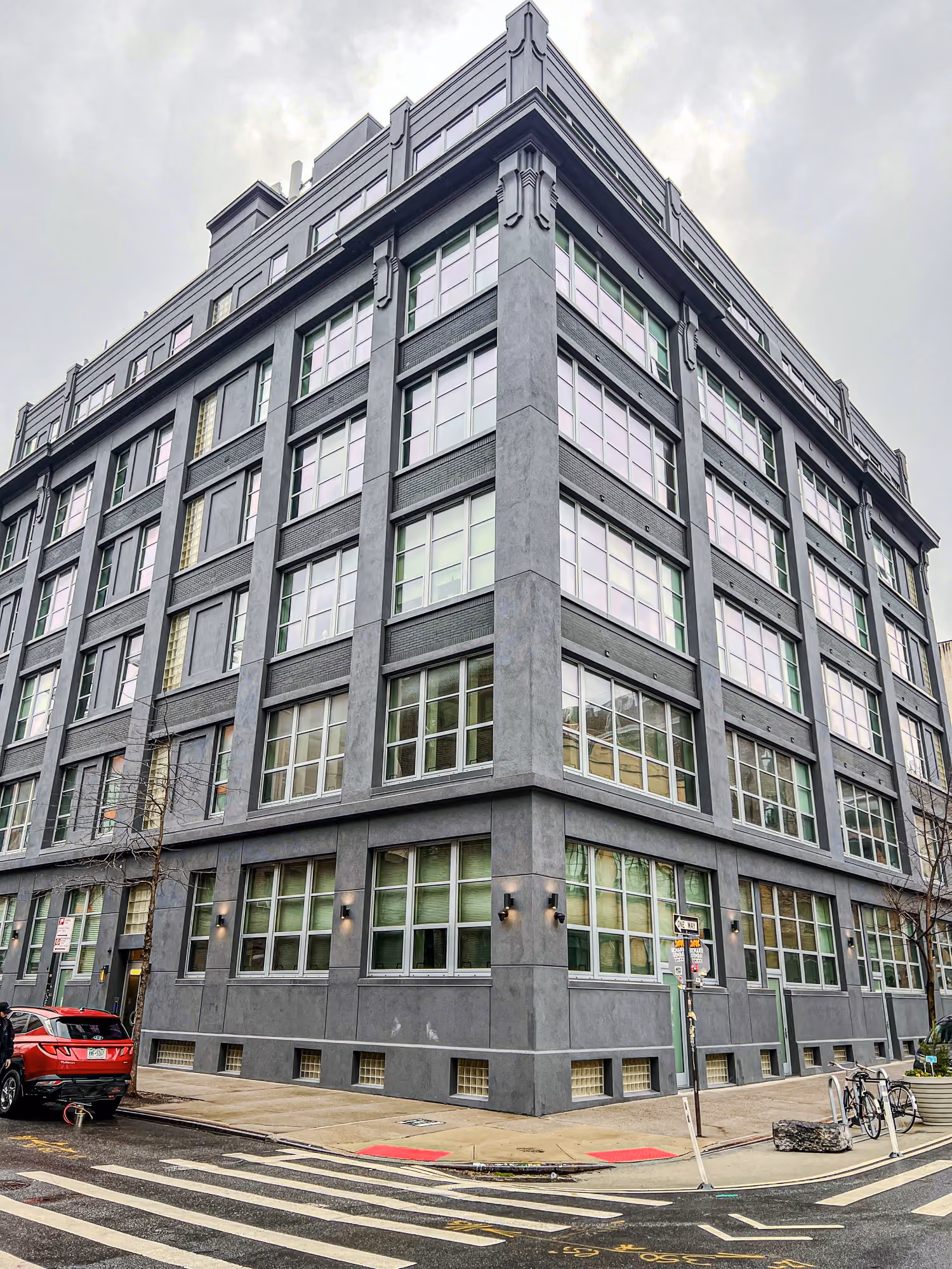 Gray multi-story building with many windows on a street corner under cloudy sky.