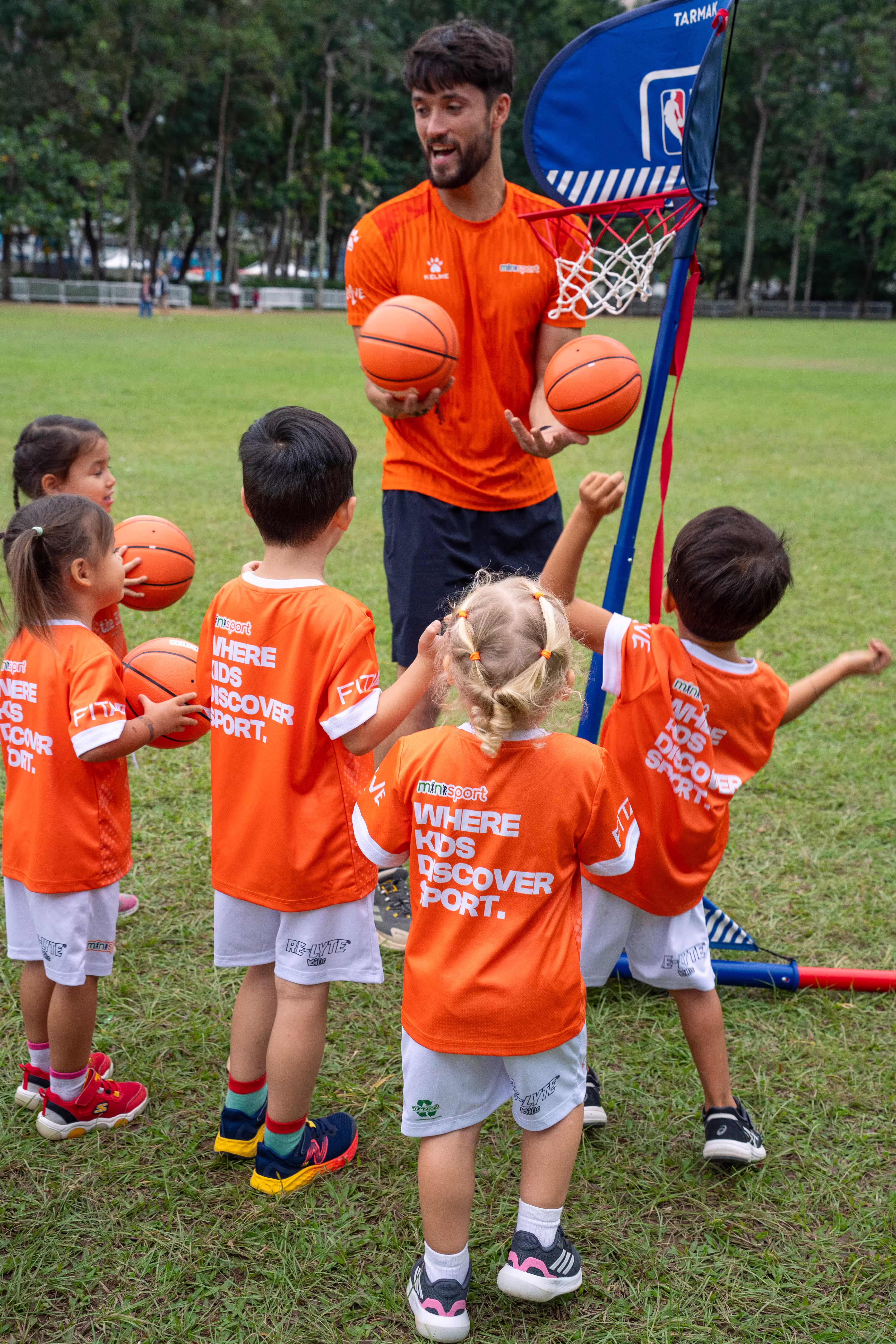 Minisport Coach speaking to kids holding basketballs in his hands