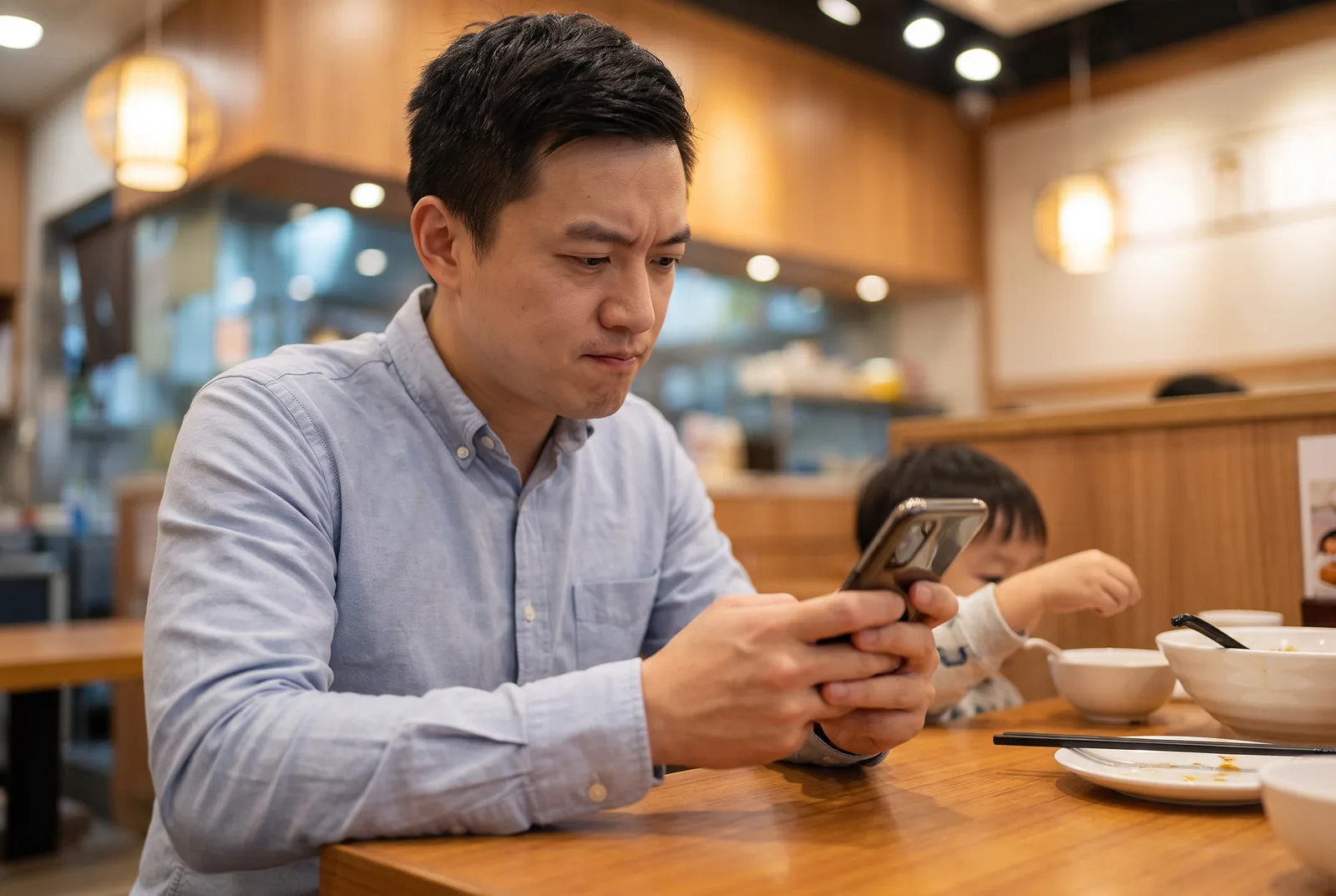 Healthy local father checking his phone at a family restaurant while his child sits nearby