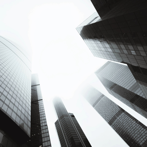Looking upward between tall modern skyscrapers against a partly cloudy blue sky.