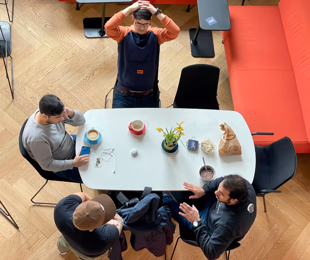 4 people sitting at a desk, having coffee and talking to each other.