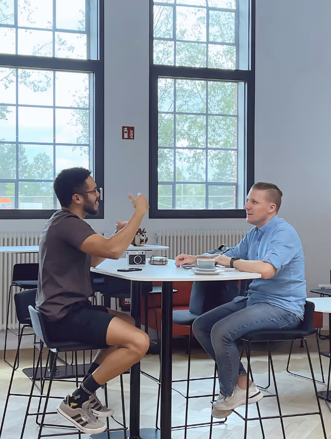 two people sitting at a desk, having a coffee and discussing.