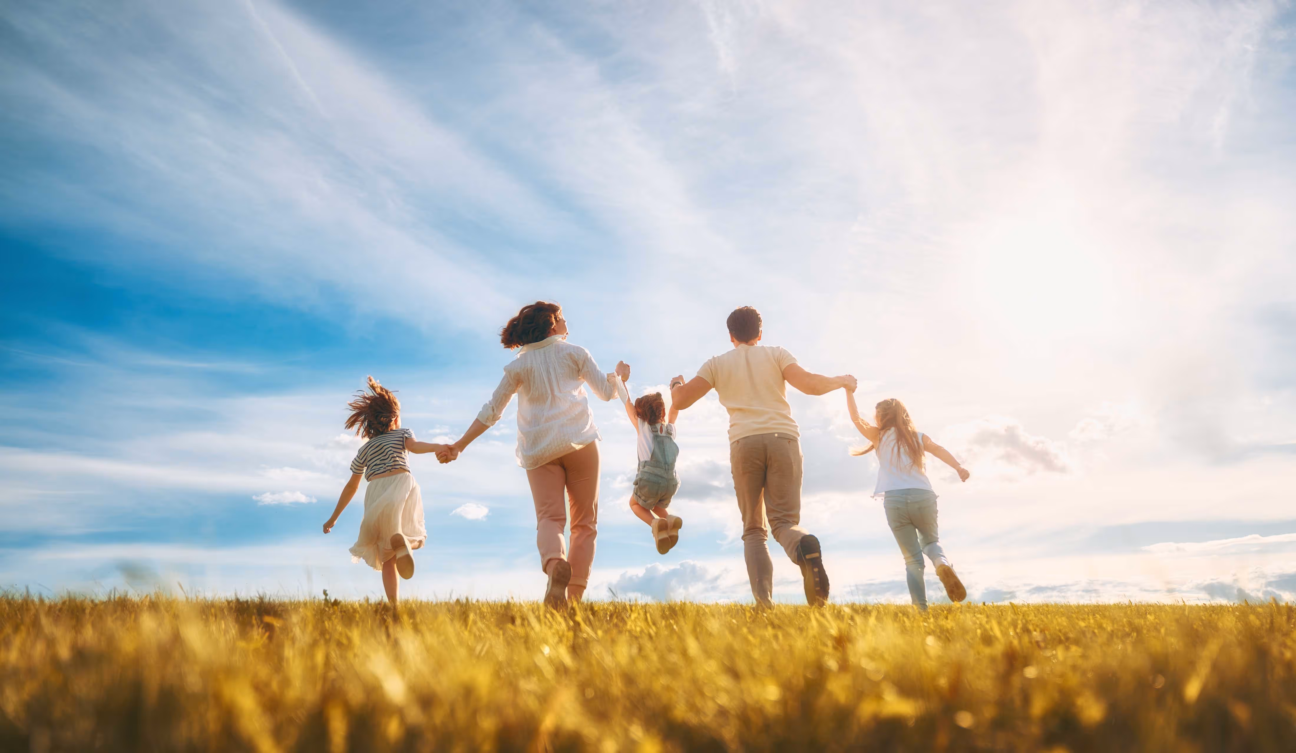 5 person family all holding hands running through a field into the light.
