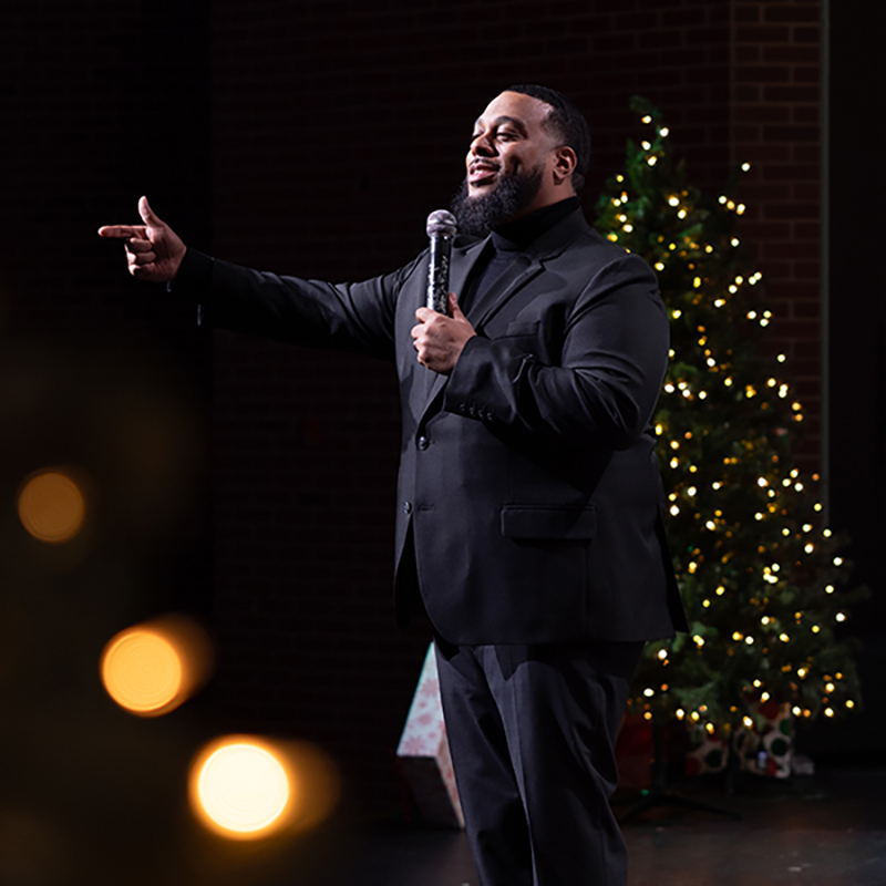 Pastor on stage in a black suit during a Christmas Experience.