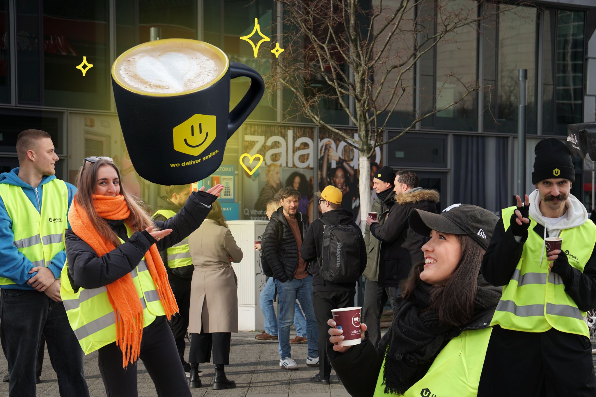 A cheerful group of Urbify employees, some in Urbify vests, enjoy coffee together at a morning pop-up event outside Zalando HQ. A large coffee cup graphic with a smiley face and the phrase “we deliver smiles” highlights the friendly, welcoming atmosphere.