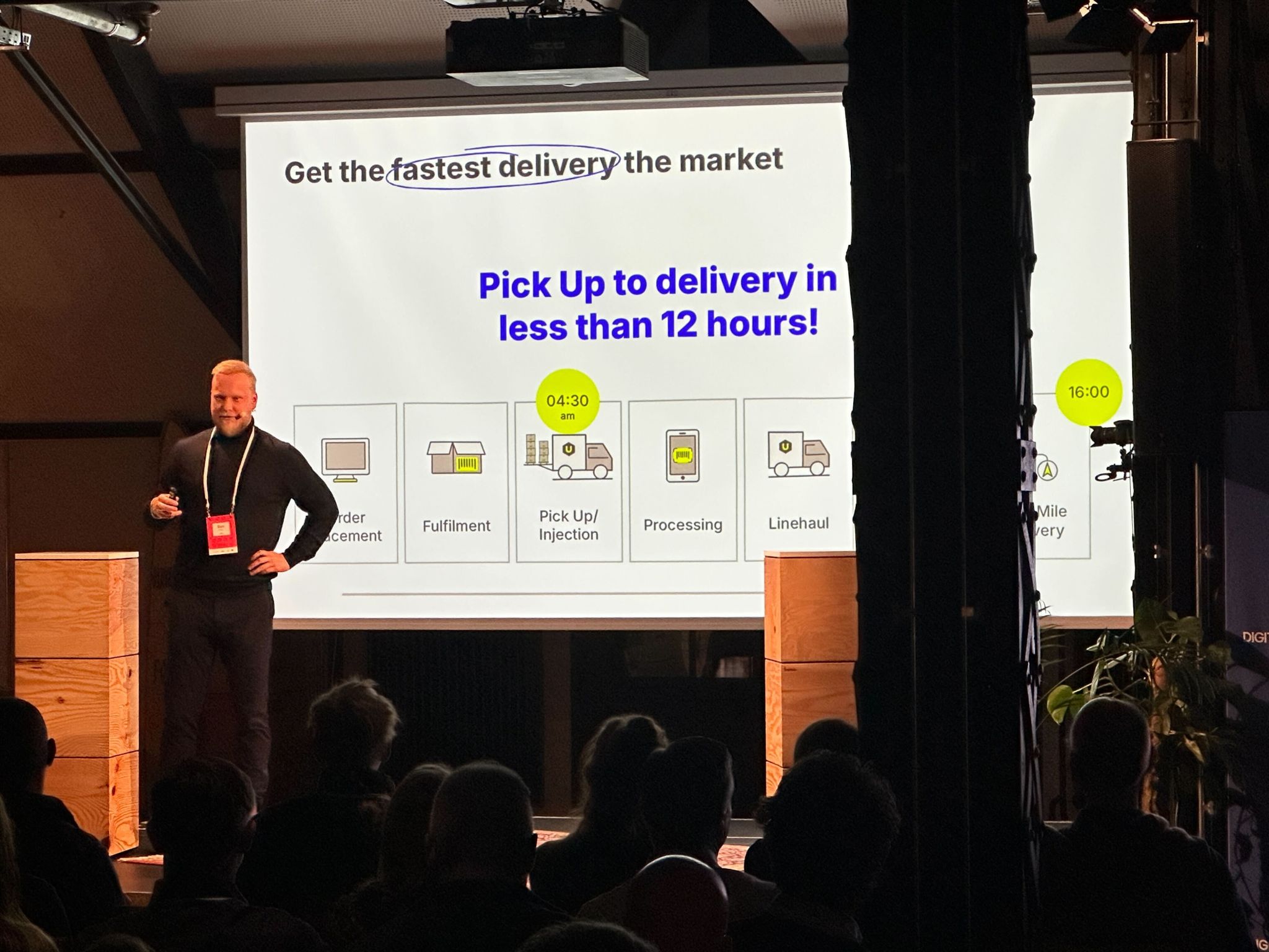 Audience view of LogisticsTech Talks event, showing the stage, podiums, and speakers under warm lighting.