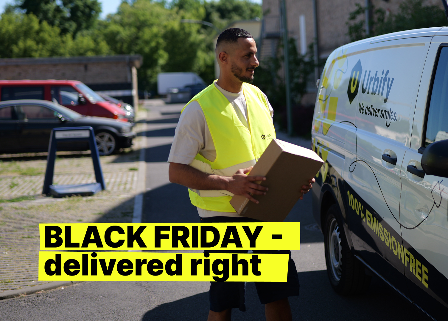  A Urbify courier in a yellow safety vest carries a package beside a van labeled “Urbify – We deliver smiles,” marked “100% emission free,” in a parking area; foreground text reads “Black Friday – delivered right.”