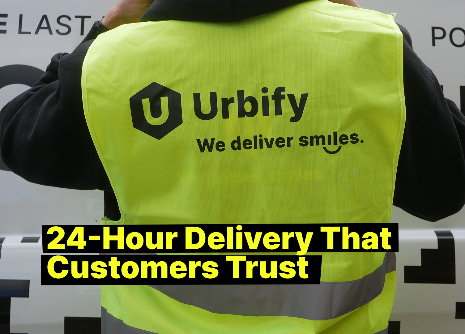 Urbify delivery driver wearing a yellow safety vest with logo and the slogan “We deliver smiles,” representing trusted 24-hour delivery service.