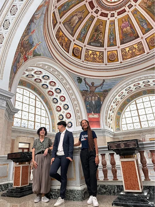 Three people standing in a room with an ornately decorated dome ceiling