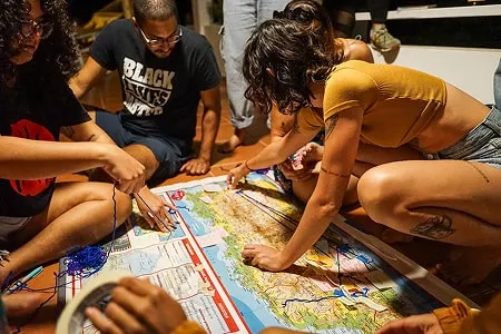 People sitting on the floor labeling a map and marking distances with string