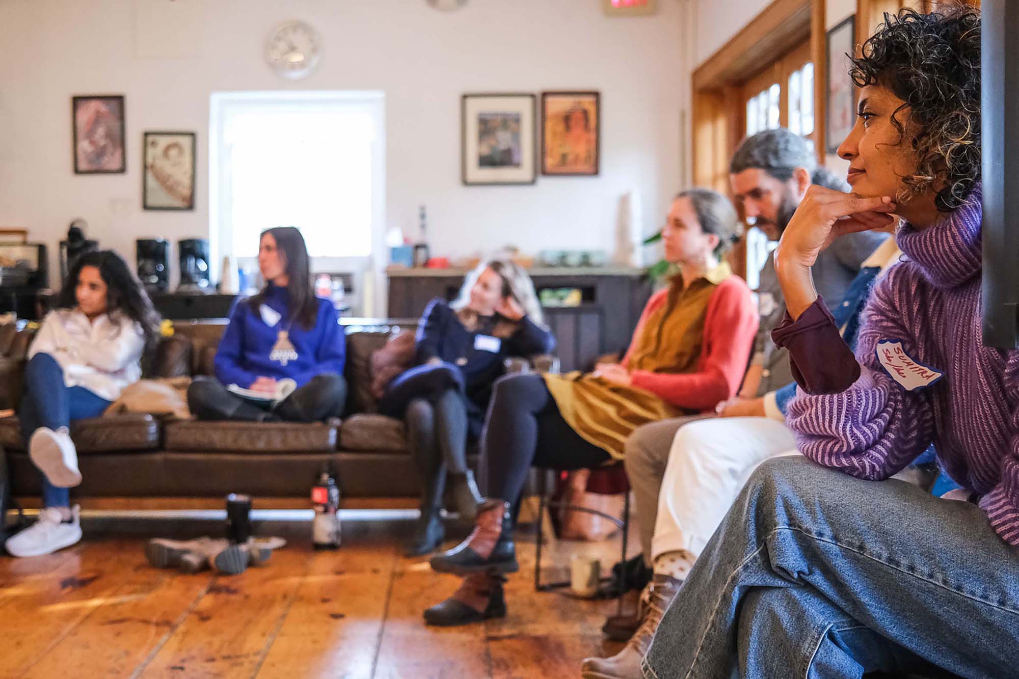 People seated in a circle of chairs and couches, listening thoughtfully to someone off-camera