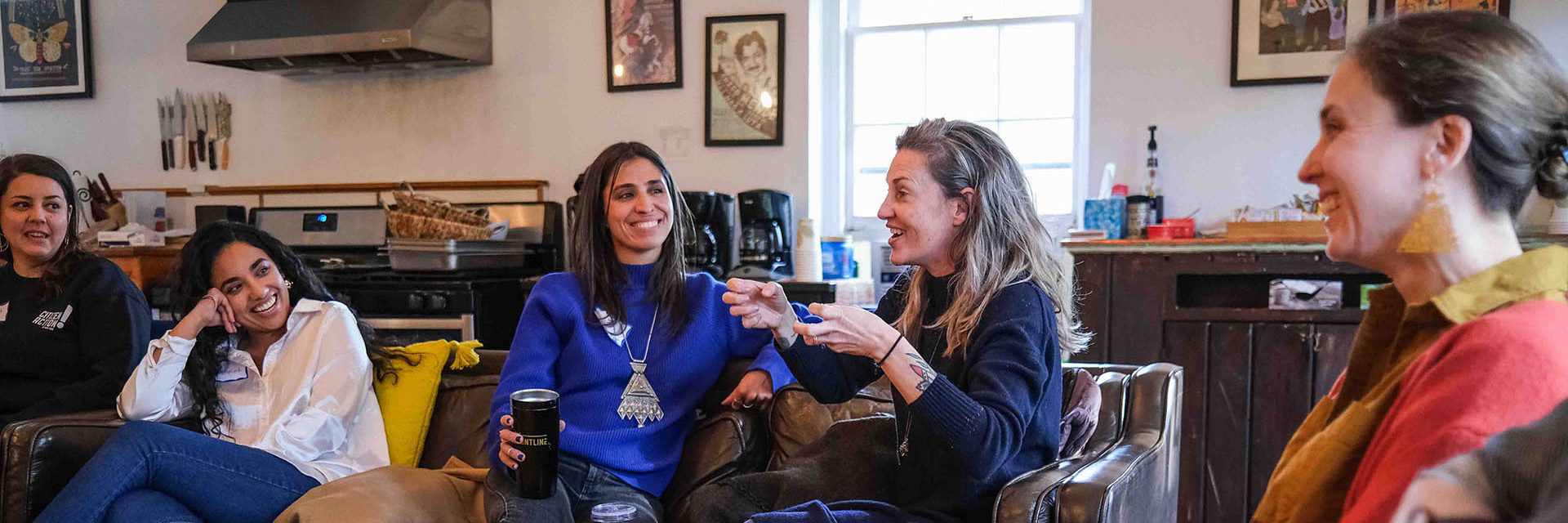 Five women sitting on a couch engaged in lively conversation