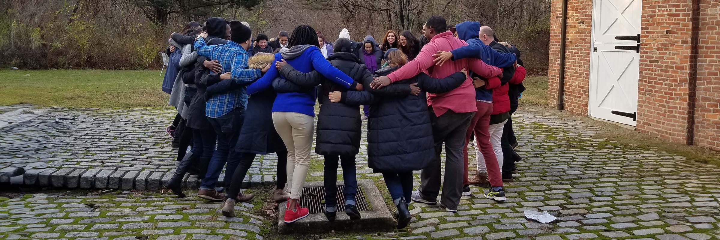 A circle of people with their arms on each others' shoulders in the Action Lab's courtyard