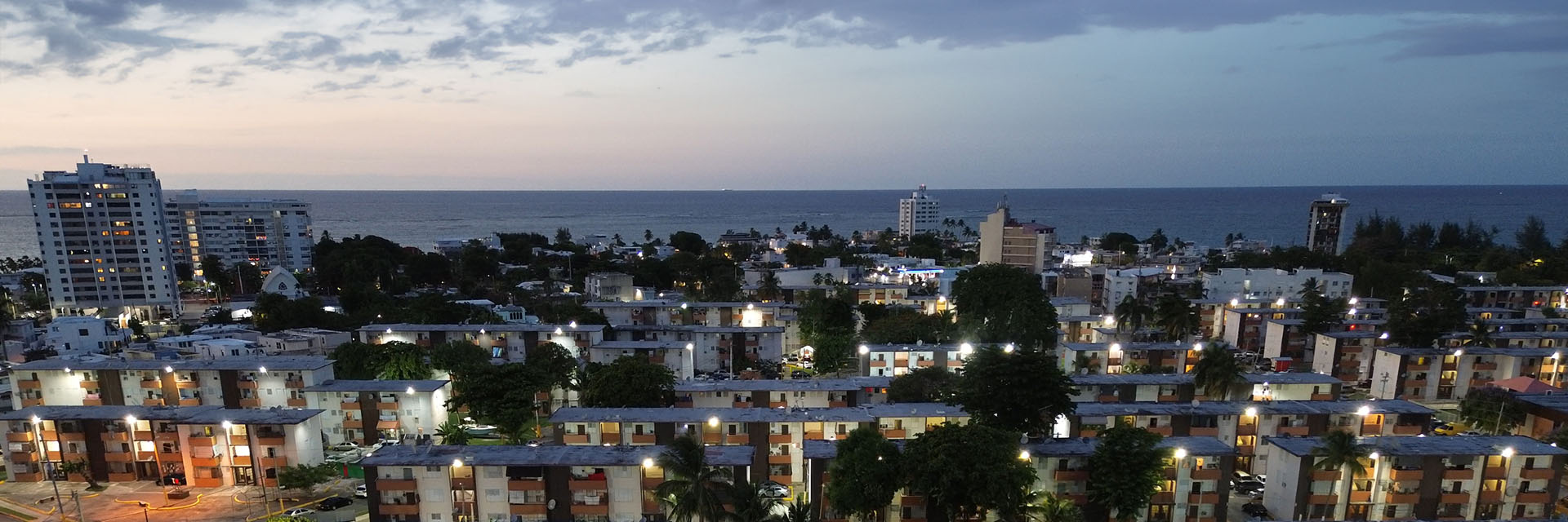 Cityscape at dusk overlooking apartment buildings and the ocean.
