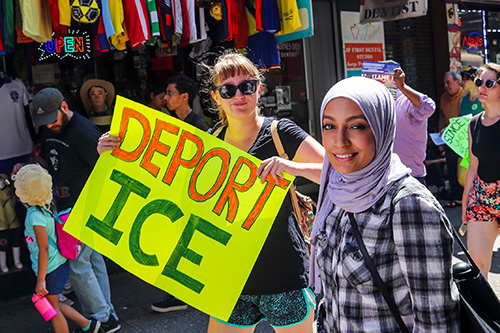 Two women at a street protest, one wearing a head scarf, one holding a sign reading “Deport ICE.”