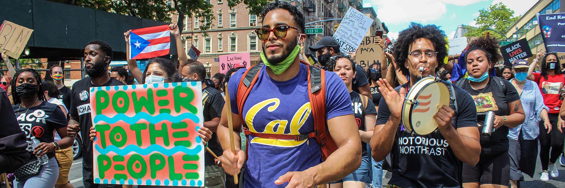 Crowd marching in a protest with Puerto Rican flags and signs reading ‘Power to the People’ and ‘Black Lives Matter.