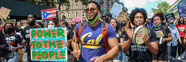 Crowd marching in a protest with Puerto Rican flags and signs reading ‘Power to the People’ and ‘Black Lives Matter.