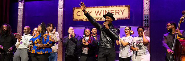 Group of performers onstage at City Winery New York City, with a singer at center raising a hand toward the audience.