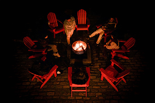 Overhead view of people sitting in red chairs around a glowing fire pit at night.