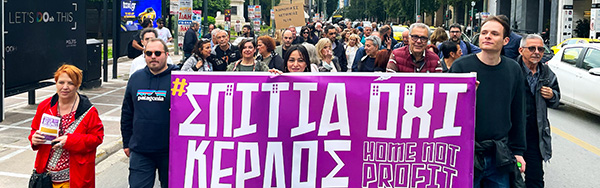 Protesters marching with a large purple banner reading “Home Not Profit” in English and Greek.
