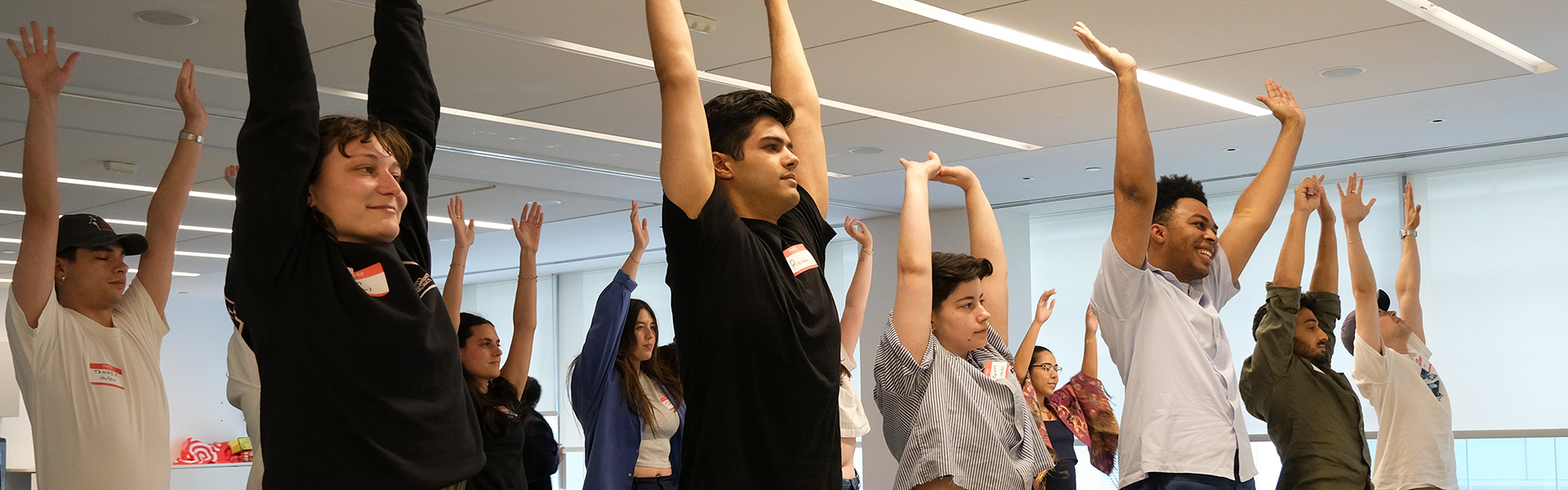 Group of people standing in a bright room with arms raised during a group activity or stretch.