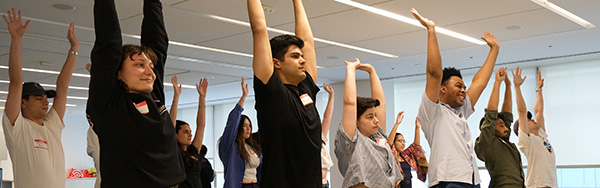 Group of people standing in a bright room with arms raised during a group activity or stretch.