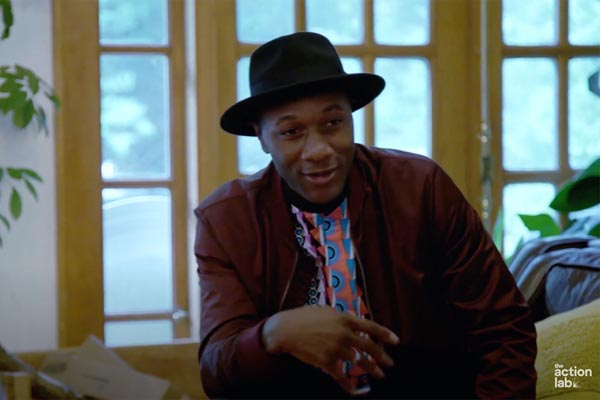 Person in a hat speaking casually in a sunlit room
