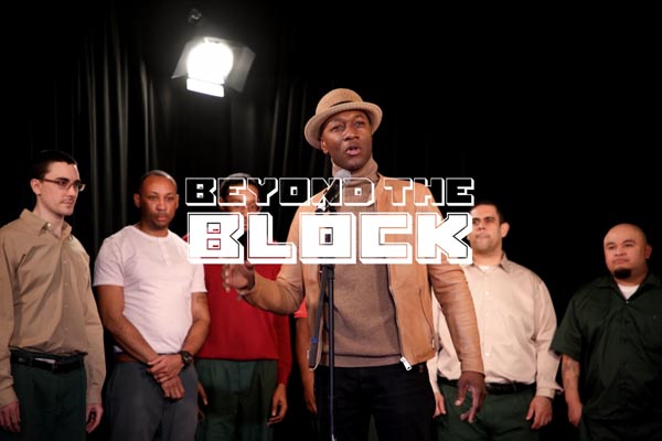 Man speaking at a microphone with a group standing behind him under the title “Beyond the Block”