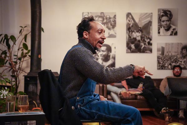 Man gestures while speaking during an indoor discussion with activist photos on the walls.