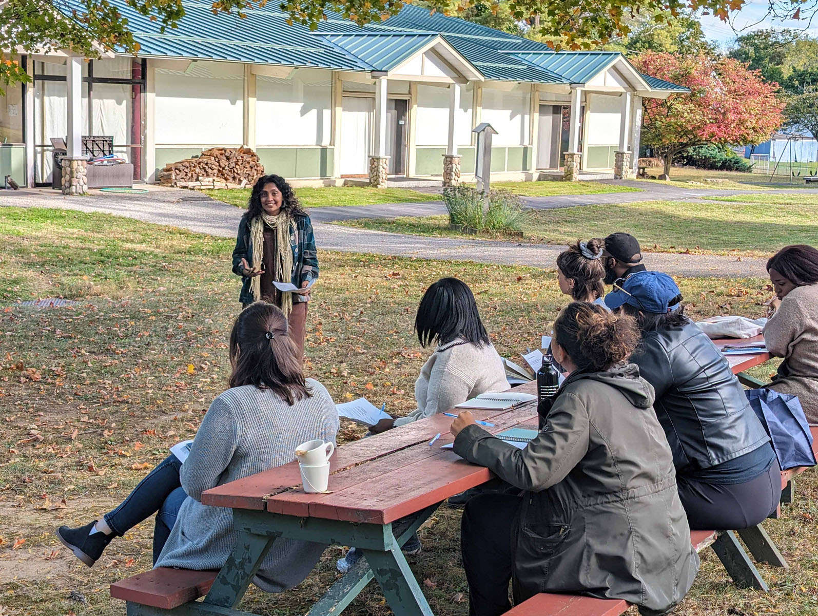 Outdoor workshop with a facilitator speaking to a group seated at picnic tables