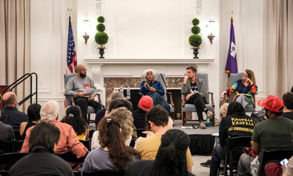 Audience listening to a four-person panel discussion in an elegant room with flags and greenery