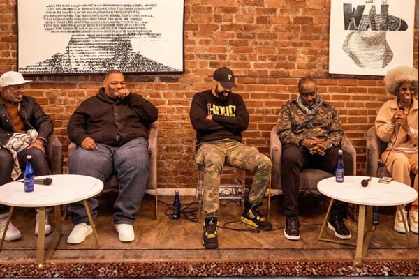 Five panelists seated before a brick wall, talking and laughing beneath framed artwork