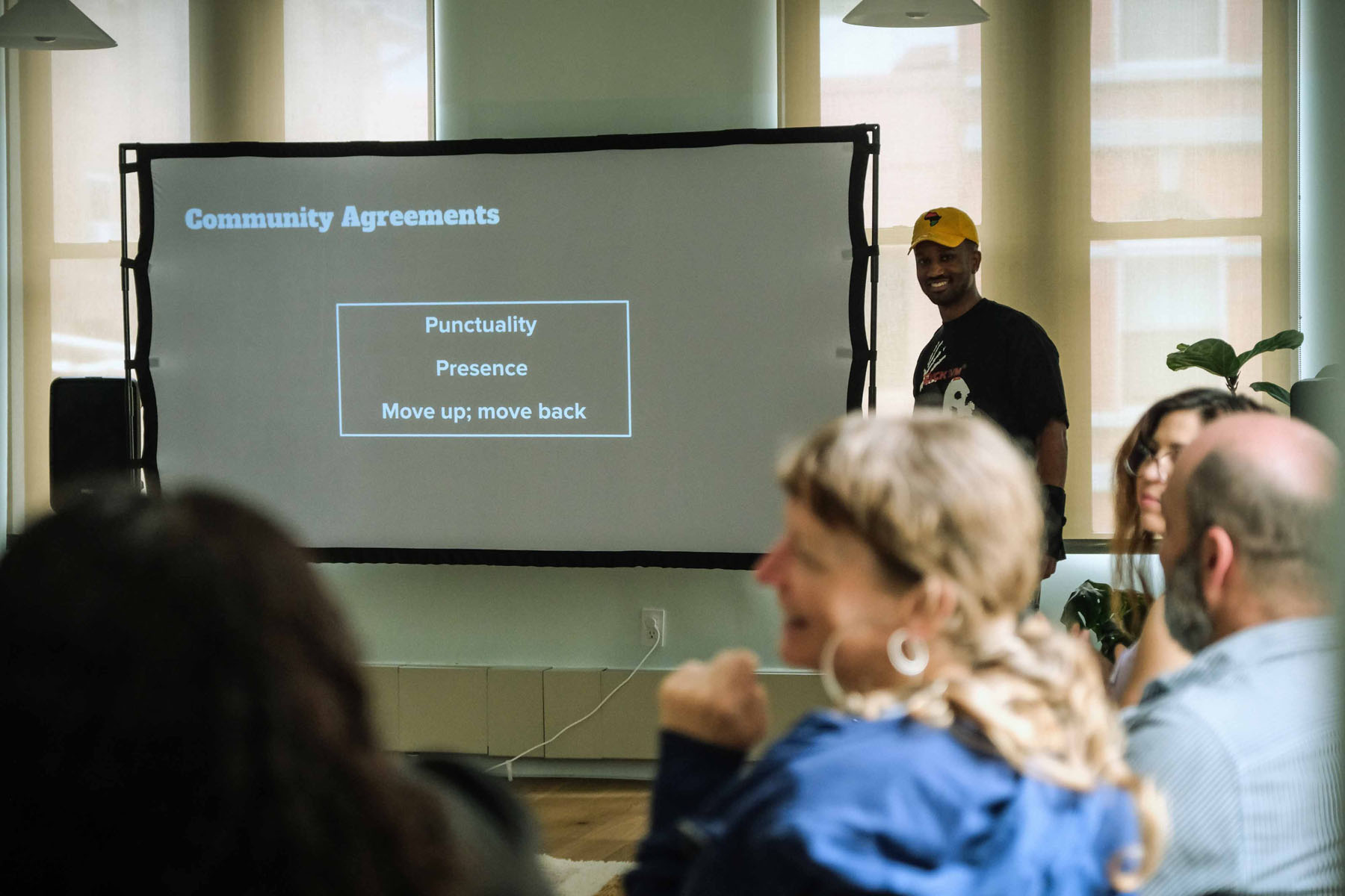 Facilitator smiling beside a projected slide listing community agreements