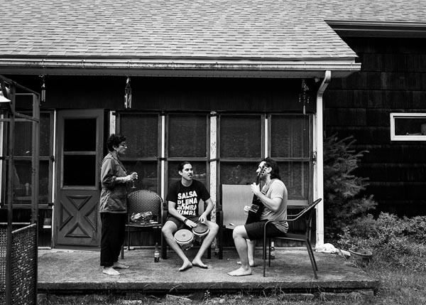 Three people gather on a porch as two play percussion and guitar.
