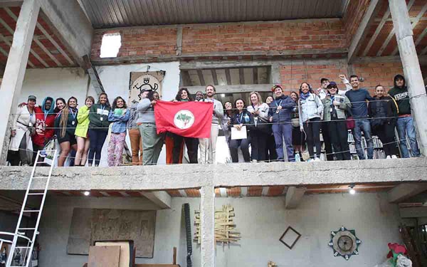 Group stands on an upper-level balcony holding a red movement flag inside an unfinished building.