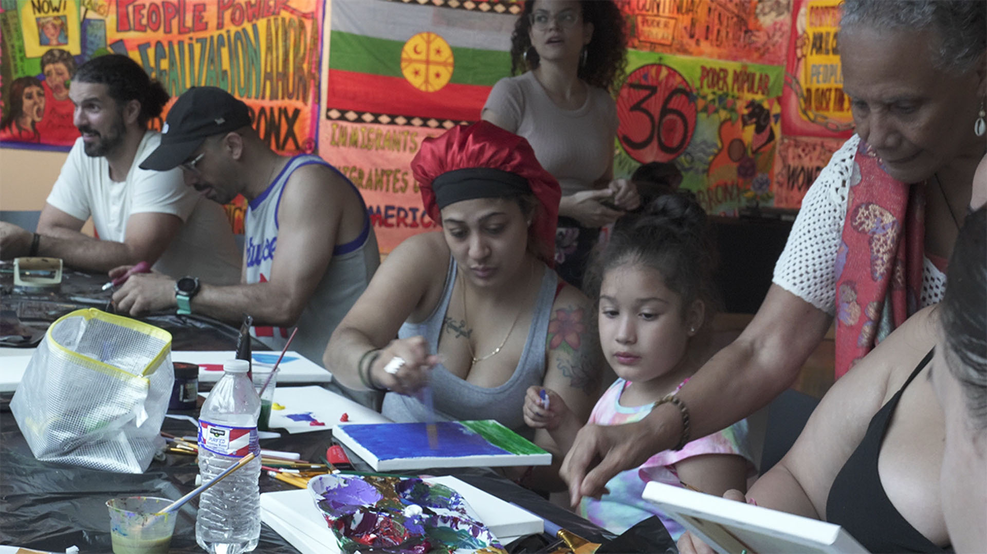 Families paint at a long table surrounded by vibrant posters and flags.