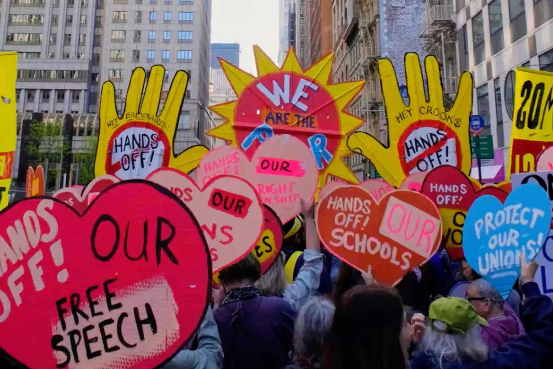 Colorful protest with large hand-shaped and heart-shaped signs demanding rights and protections