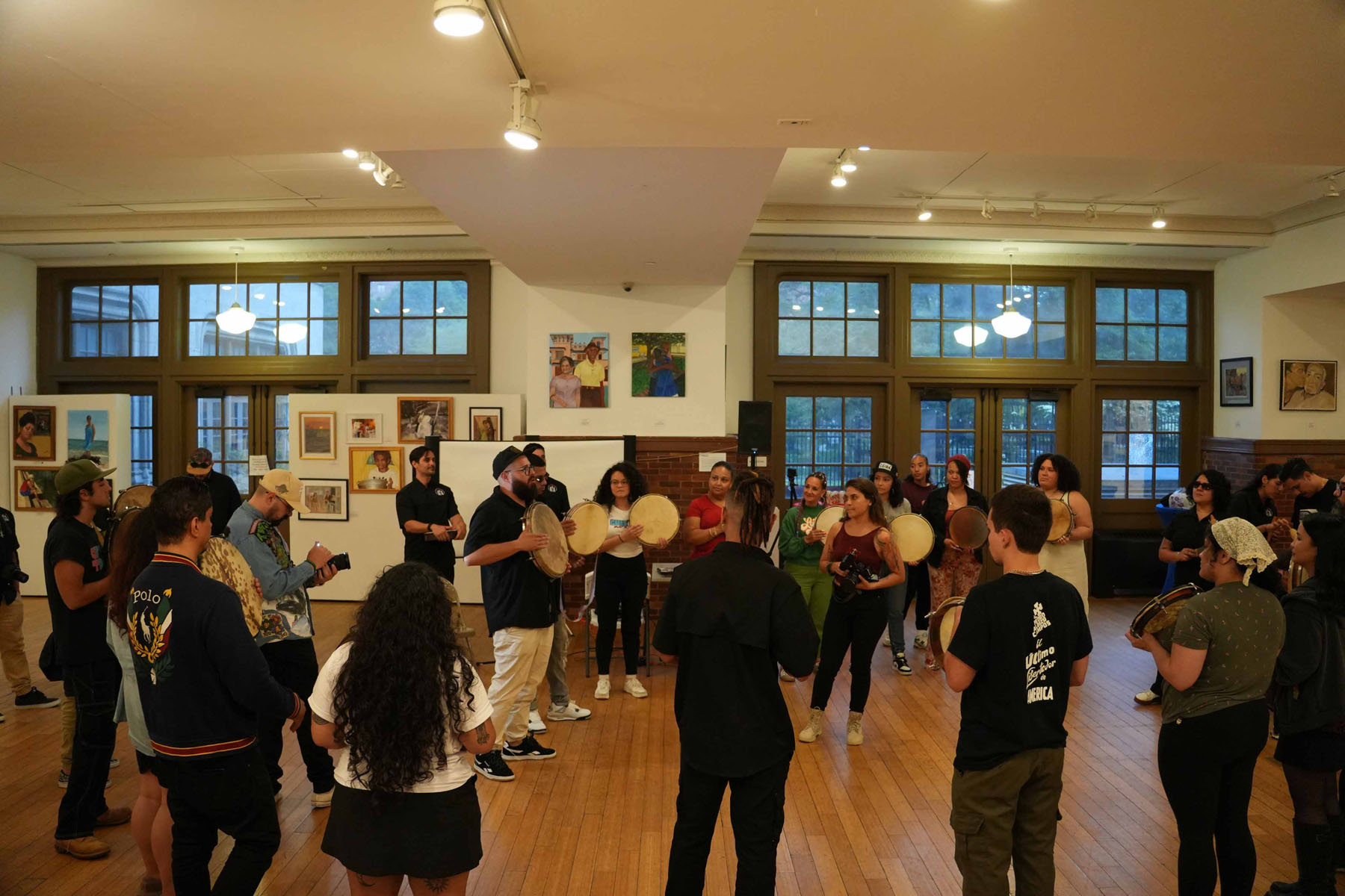 Large circle of people drumming and singing together in a bright community room