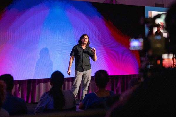 Speaker presenting onstage before a vivid purple and blue LED backdrop