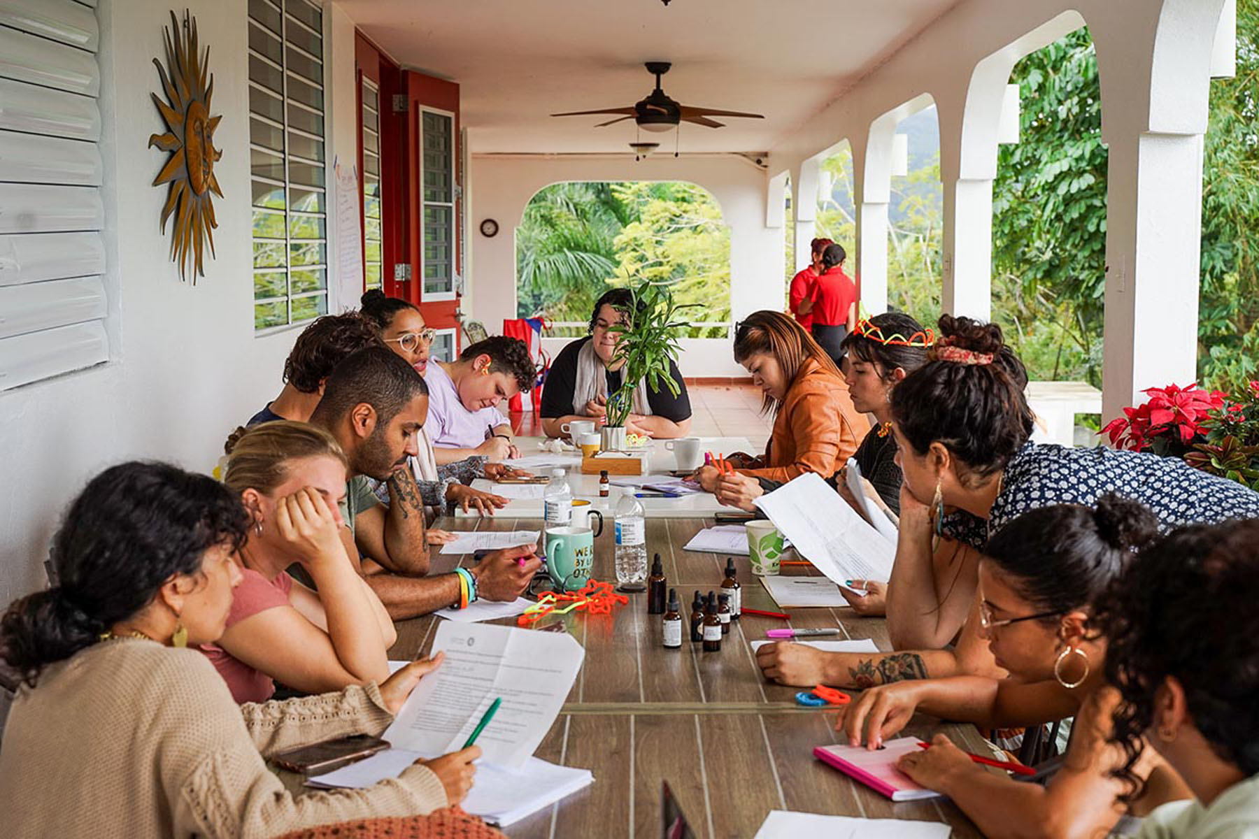 Participants sit around a long porch table engaged in discussion and note-taking.