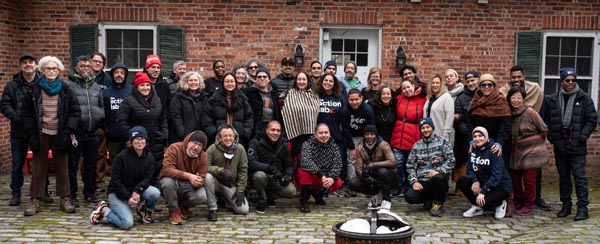 Large group of people gathered outside a brick building, smiling and posing together in winter clothing. 