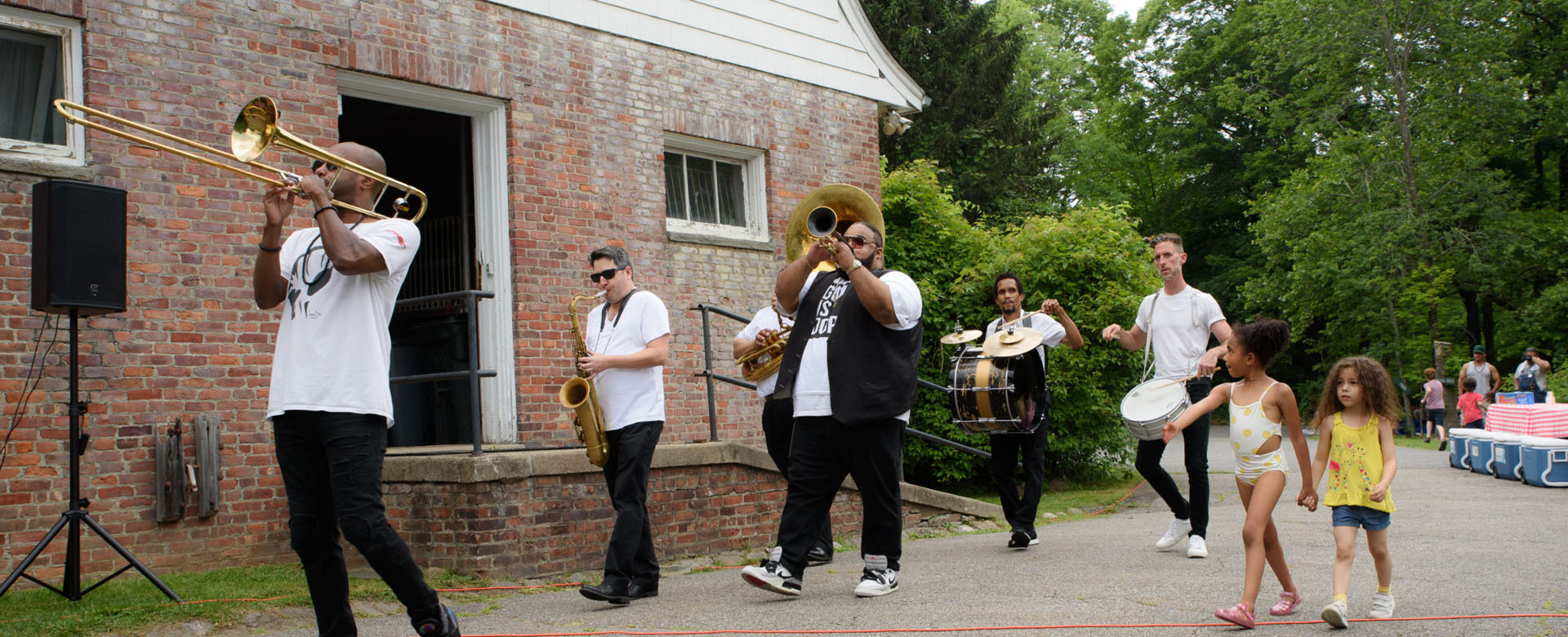 Photo of a brass band marching outside a brick building as two children walk alongside them.