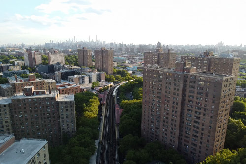 Aerial view of city apartment buildings with train tracks running between them toward the skyline.