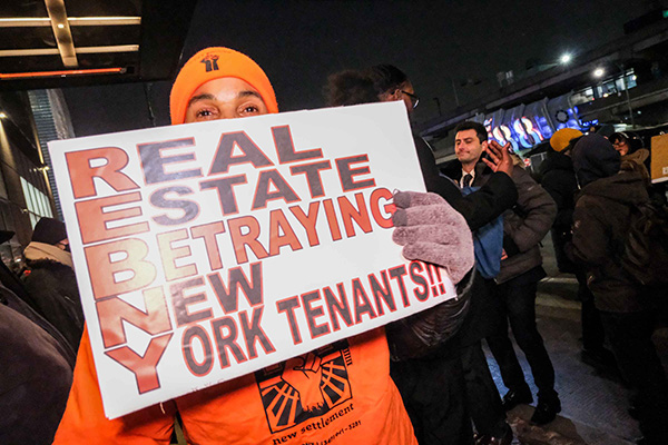 Person raising a sign saying ‘Real estate betraying New York tenants.’