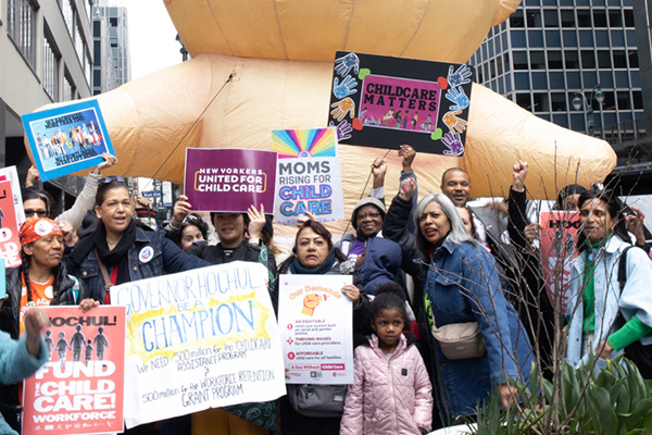 Large crowd marching with a giant inflatable baby and ‘Childcare Matters’ signs