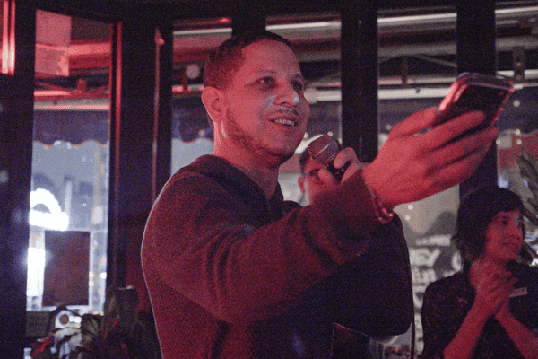 Jesus Gonzalez, Director of the Evergreen Initiative, giving a speech wearing a black hoodie. Mic in left hang and stretched out right hand with phone.