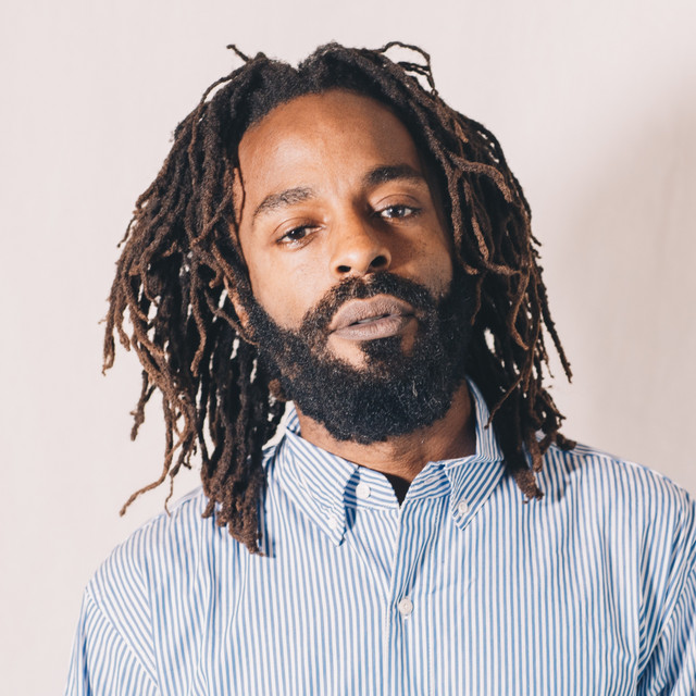 Headshot of John Forte, African American man with short locks and wearing a blue and white striped oxford shirt.