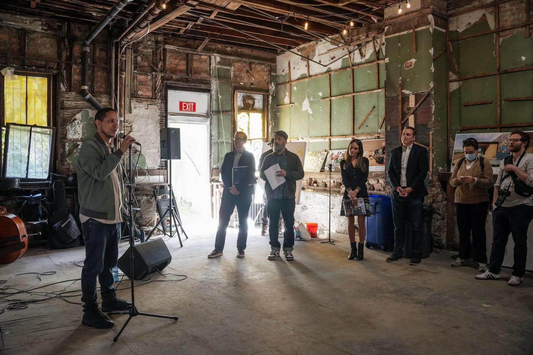 A person speaking on a microphone to a group of people in a raw building space.